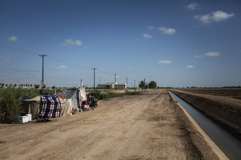 This July 24, 2020, photo shows a homeless encampment near a canal in El Centro, Calif. As support services have dwindled amid the COVID-19 pandemic, some homeless people in Imperial County have resorted to bathing in irrigation canals. Homelessness looks different in different parts of the U.S., especially in rural agricultural regions such as Imperial County. Image by Anna Maria Barry-Jester/KHN and the Howard Center For Investigative Journalism via AP. United States, 2020.