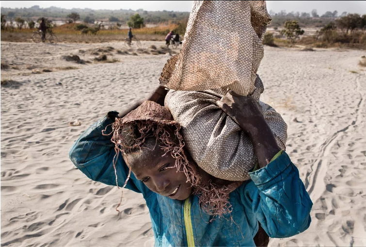 Daniel (11) carries a bag of cobalt on his back. He works in a mine ferrying sacks of cobalt to a depot. Image by Sebastian Meyer. Democratic Republic of Congo, 2018.