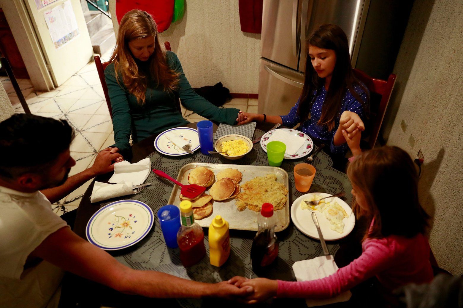 The family prays before a meal. It was breakfast for dinner, including pancakes. Image by Erika Schultz. Mexico, 2019. 