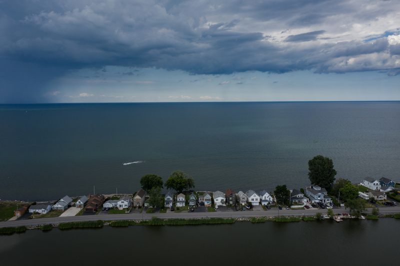 Houses are shown along Edgemere Drive on Lake Ontario and Cranberry Pond in Greece, New York, on July 28, 2020. Homeowners here have paid to put large boulders in front of their property to prevent erosion. The area is particularly susceptible to flooding because it receives storm surge from Lake Ontario to the north and flooding from a series of coastal ponds to the south. Image by Zbigniew Bzdak/Chicago Tribune. United States, 2020.
