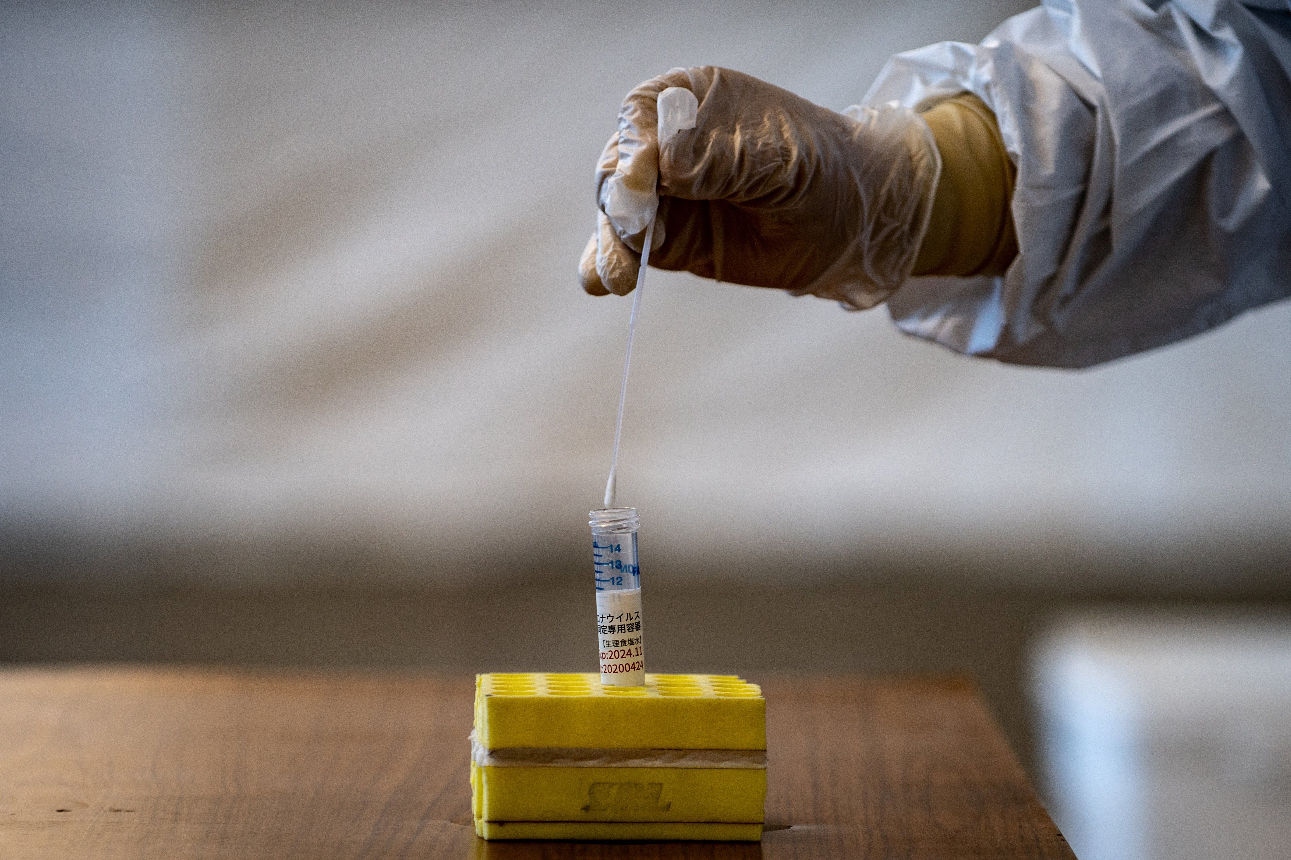 A medical staff member wearing protective clothing puts a swab into a container during demonstration of the Polymerase Chain Reaction (PCR) swab test for COVID-19 in Tokyo on May 8, 2020. Image by Philip Fong/AFP. Japan, 2020.