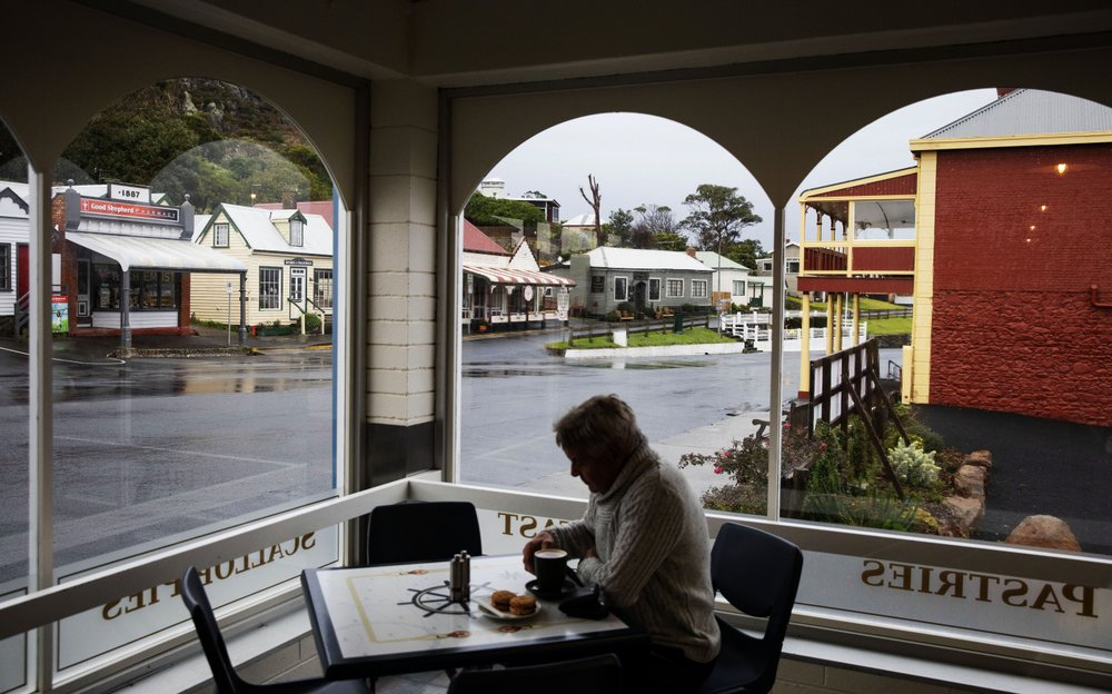 Shops line a street in the town of Stanley as a patron sips a cup of coffee in Tasmania, Australia, Tuesday, July 23, 2019. Like America's Appalachia, Tasmania is the country's epicenter for opioids. It has the nation's highest rate of opioid packs sold per person _ 2.7 packs each. One region has the highest number of government-subsidized opioid prescriptions in Australia: more than 110,000 for every 100,000 people. Image by David Goldman. Australia, 2019.