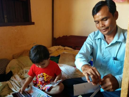 Journalist Sa Piseth at home with his son, going through photos of illegal logs. Image by Saul Elbein. Cambodia, 2014.