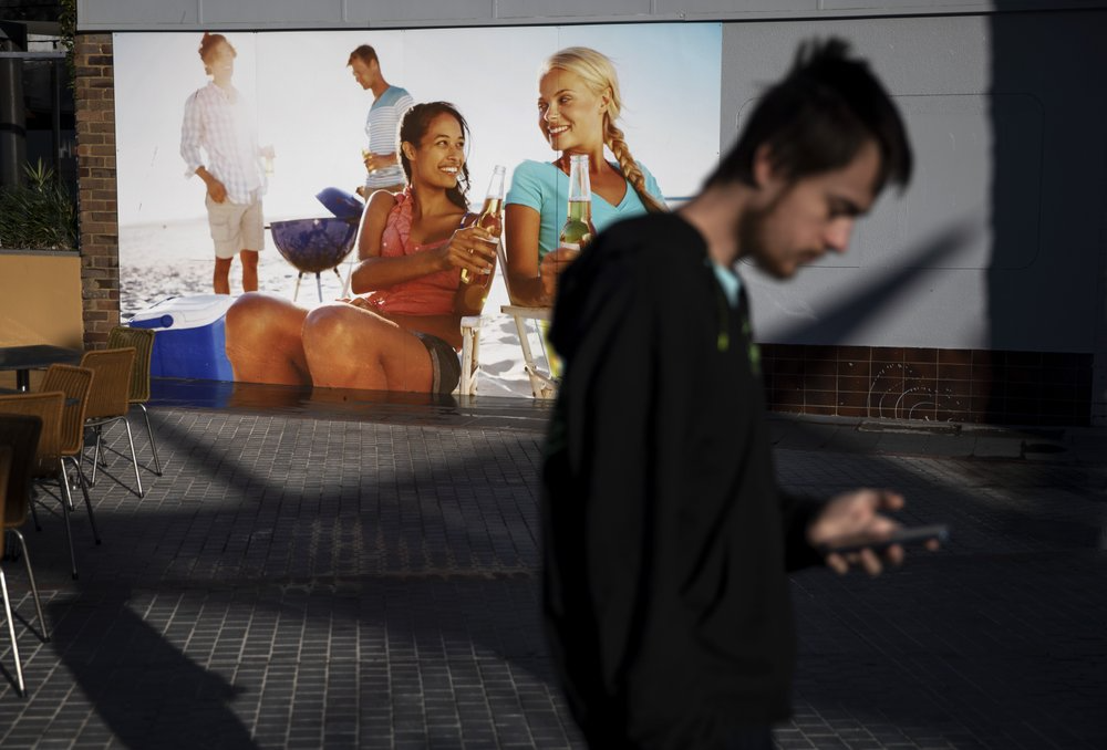 Sam Ware, 22, walks past a billboard while out on a morning walk from the hostel where he is staying at The Entrance, Central Coast, Australia, Thursday, July 25, 2019. Sam lost friends and family and most of his belongings through his addiction. His phones, laptop and clothes were left behind or stolen while overdosing on trains, in shopping centers, in a library. Image courtesy of David Goldman. Australia, 2019.