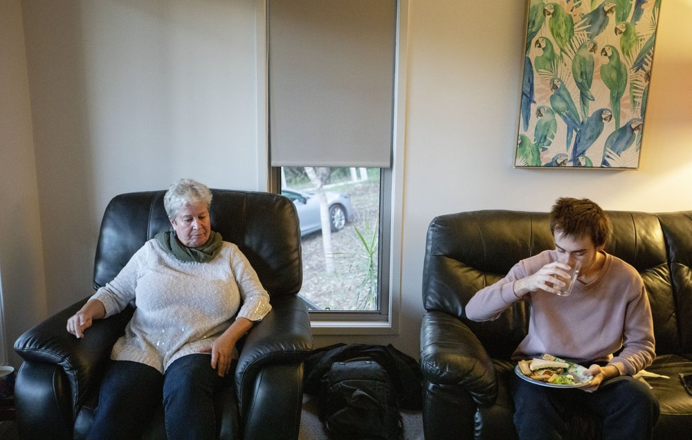 Sam Ware, 22, eats as his mother, Deb Ware, sits by, upon letting him return to her home for the first time since he last overdosed, in Fountaindale, Central Coast, Australia, Friday, July 19, 2019. Deb lets Sam inside, into the warmth of the living room. He sits on the couch where he overdosed three weeks earlier and wolfs down a sandwich, and toast, and cereal, and cookies. Deb sinks into her armchair, looking broken. Image courtesy of David Goldman. Australia, 2019.