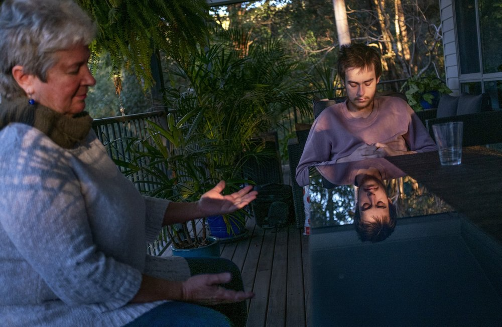 Sam Ware, right, claps as his mother, Deb Ware, finishes a song on the guitar at her home in Fountaindale, Central Coast, Australia, Friday, July 19, 2019. Sam was close to his mother, who had raised him on her own since he was a toddler, and who shared his fondness for music and the beach. Only three weeks earlier she said goodbye as doctors placed him into an induced coma, as a tsunami of opioids and other drugs roared through his battered body. Image courtesy of David Goldman. Australia, 2019.