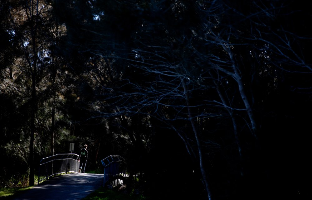 Sam Ware, 22, steps into a ray of sunlight while walking through a park in The Entrance, Central Coast, Australia, Thursday, July 25, 2019. His mother, Deb, watched the kind-hearted, funny boy she loved rapidly disappear as his opioid addiction took hold. In his place was a deceptive, desperate stranger whose soul seemed to have been sucked from his body. Looking back now, she marvels at how fast it all happened. "You become the drug," she says. "It's only a matter of five days before Sam was gone. "Image courtesy of David Goldman. Australia, 2019.