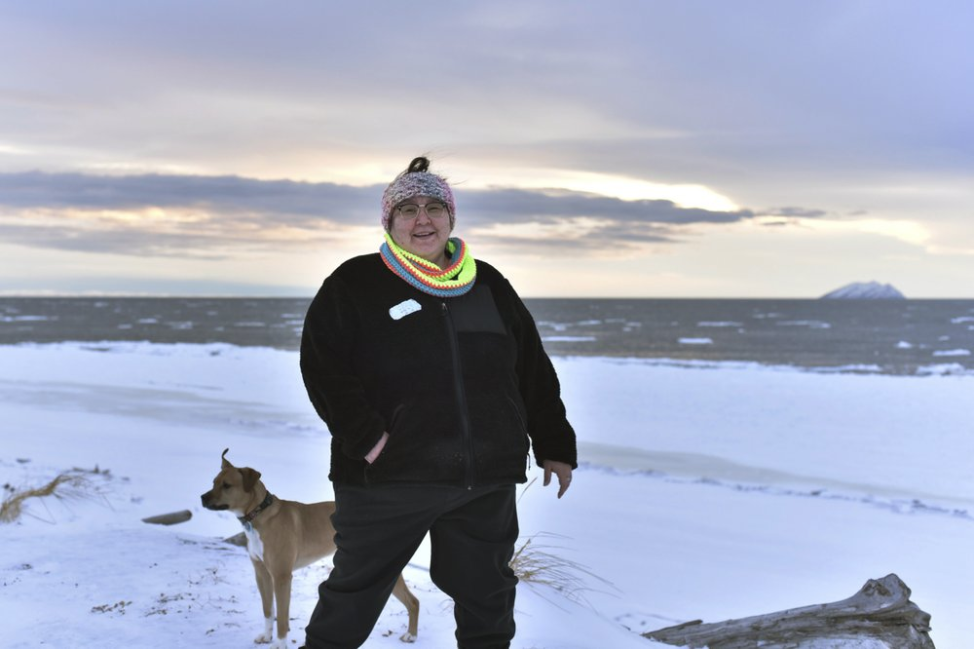 In this Jan. 14, 2019 photo, Clarice "Bun" Hardy stands on the beach with her dog, Marley, in the Native Village of Shaktoolik, Alaska. Hardy, a former 911 dispatcher for the Nome Police Department, says she moved back to her village after a sexual assault left her feeling unsafe in Nome. Image by Wong Maye-E. United States, 2019.