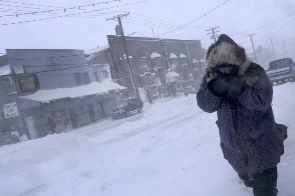 In this Feb. 23, 2019, photo, a woman shields her face from the wind during a snow storm as she walks on Front Street in Nome, Alaska. Image by Wong Maye-E. United States, 2019.