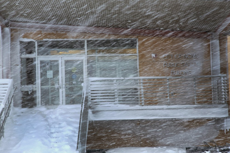 In this Feb. 22, 2019, photo, snow blows in front of the entrance to the Nome Public Safety Building, located on a tundra road on the outskirts of Nome, Alaska. According to city officials, several cabinets of police records were either lost or destroyed in the move to this building a decade ago. Image by Wong Maye-E. United States, 2019.