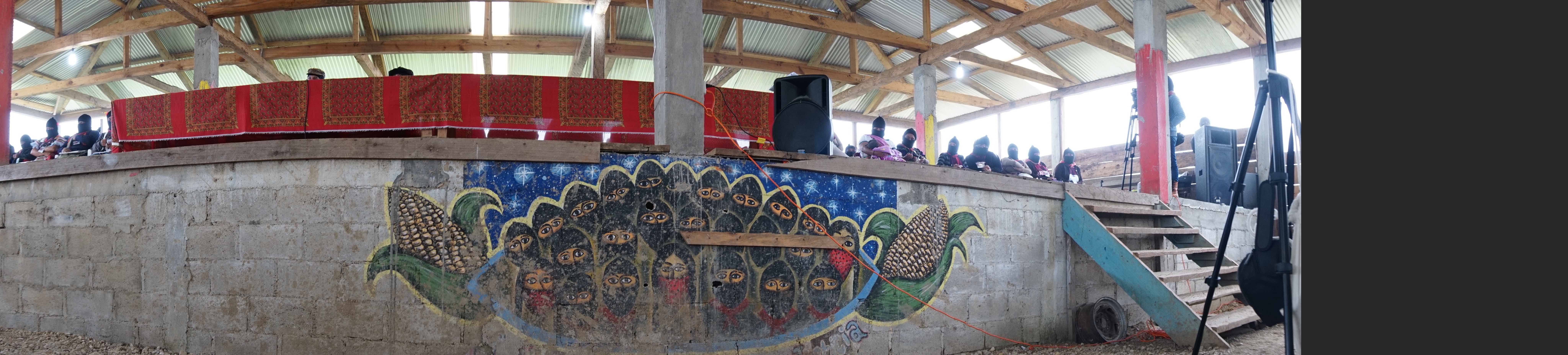 Before the stage where the high council members of the Zapatista movement sit lies a mural on which the black-masked faces of anonymous Zapatistas stare out at the world, their penetrating gazes flanked by two shucks of maize—a symbol for the earth and a life lived close to the land. Image by Jared Olson. Mexico, 2018.