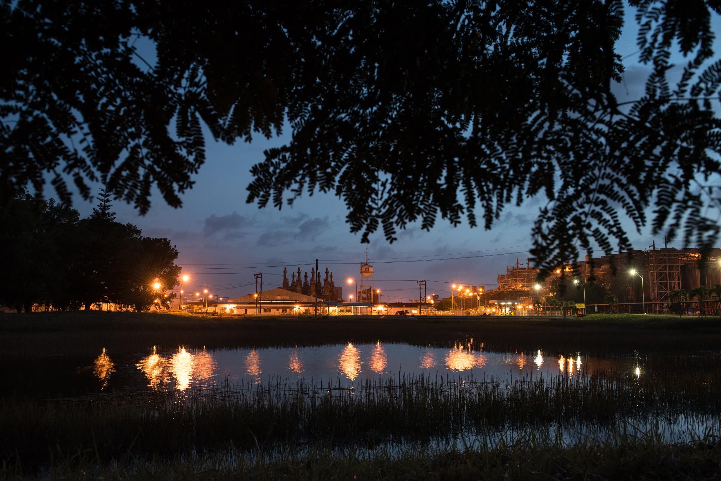 The sky at dusk is cut by the orange glow of the refinery at the Paranam Operations for Suralco, a subsidiary of Alcoa. The plant is no longer operational. Image by Stephanie Strasburg/Pittsburgh Post-Gazette. Suriname, 2017.