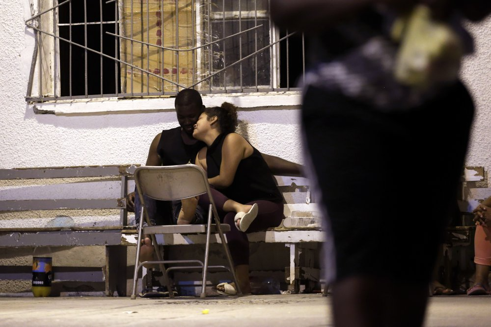In this July 28, 2019, photo, a woman from Nicaragua embraces a man from Africa under the patio floodlights at El Buen Pastor shelter for migrants in Cuidad Juarez, Mexico. Image by Gregory Bull. Mexico, 2019.