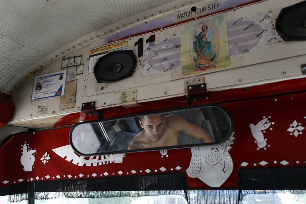 In this July 31, 2019, photo, a migrant from Cuba passes the day listening to music in a converted school bus parked near El Buen Pastor shelter for migrants in Cuidad Juarez, Mexico. Image by Gregory Bull. Mexico, 2019.