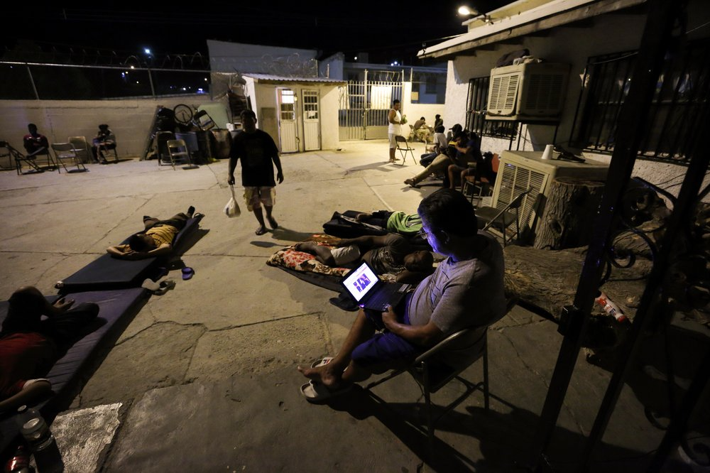 In this July 25, 2019, photo, a Cuban man looks at a computer screen as others lay around the patio at El Buen Pastor shelter for migrants in Cuidad Juarez, Mexico. Image by Gregory Bull. Mexico, 2019.