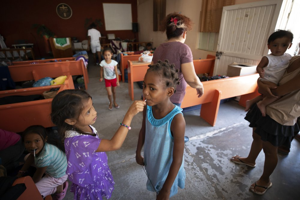 In this July 25, 2019, photo, a Honduran girl shares a lollipop with an African girl at El Buen Pastor shelter for migrants in Cuidad Juarez, Mexico. Image by Gregory Bull. Mexico, 2019. 
