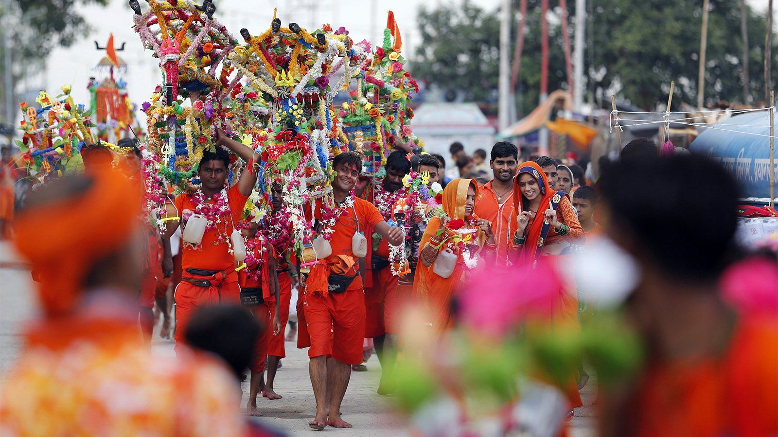 Hindu pilgrims, known as Kanwarias, walk near the banks of the Ganges River in Prayagraj, India, on July 25, 2019. Kanwarias are devotees performing a ritual pilgrimage in which they walk the roads of India, clad in saffron, and carrying ornately decorated canisters of sacred water from the Ganges River over their shoulders to take back to Hindu temples in their hometowns, during the Hindu lunar month of Shravana. Image by Rajesh Kumar. India, 2019.