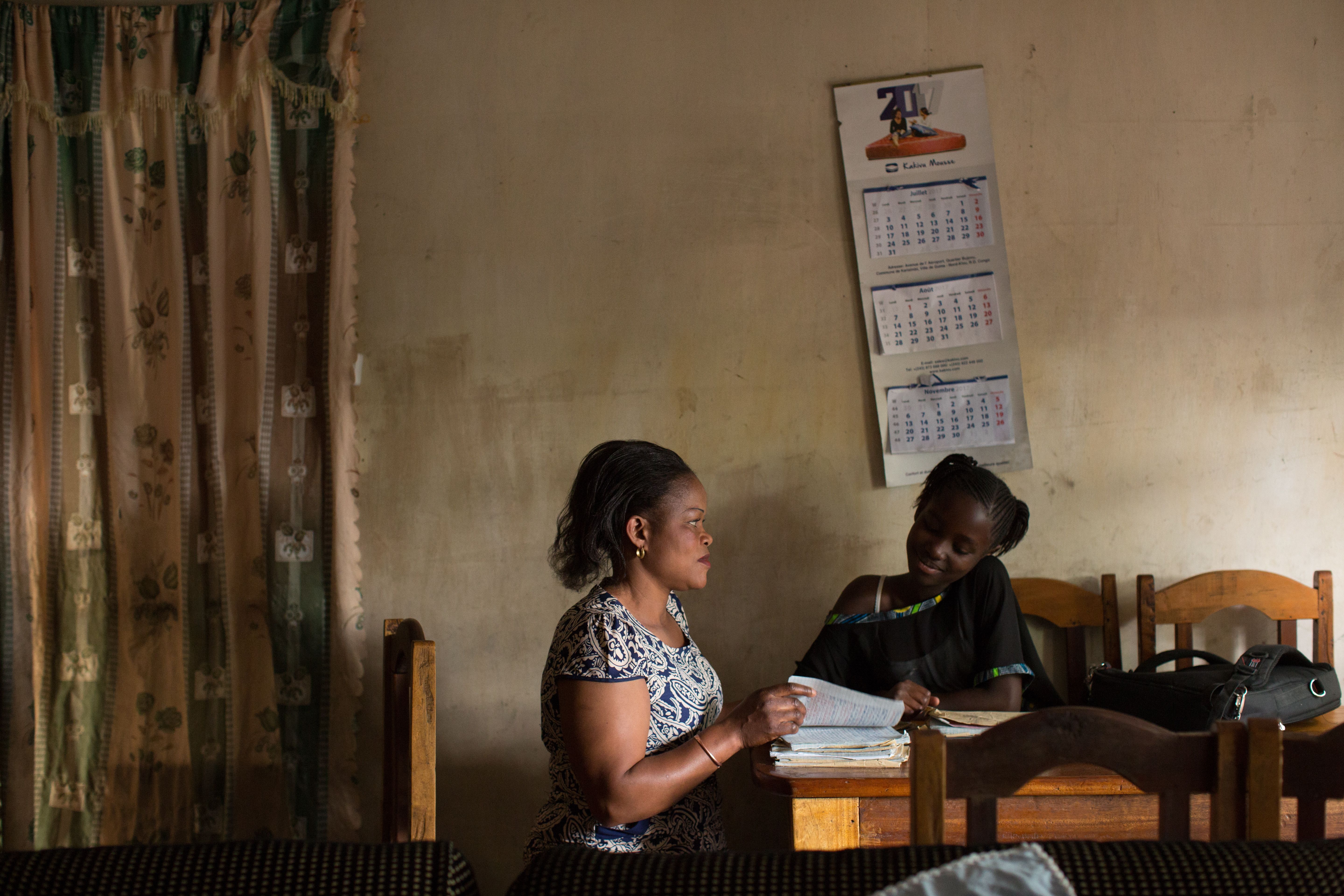 FARDC captain Fanni Katora, 34, looks over the school work of her daughter Syntiche, 10, after work at their home in Goma, D.R. Congo, November 29, 2017. Image by Allison Shelley. Democratic Republic of Congo, 2017. 