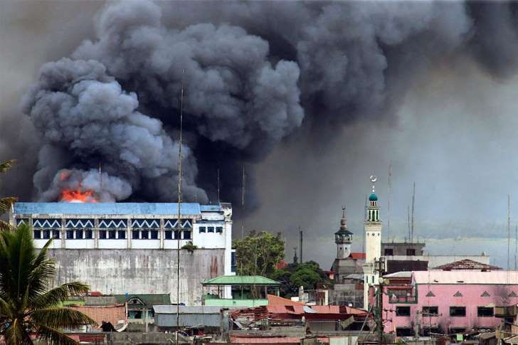 A building in Marawi is set ablaze by airstrikes carried out by the Philippine Air Force. Image by Mark Jhomel from Wikicommons. Philippines, 2017. (CC BY-SA 4.0)