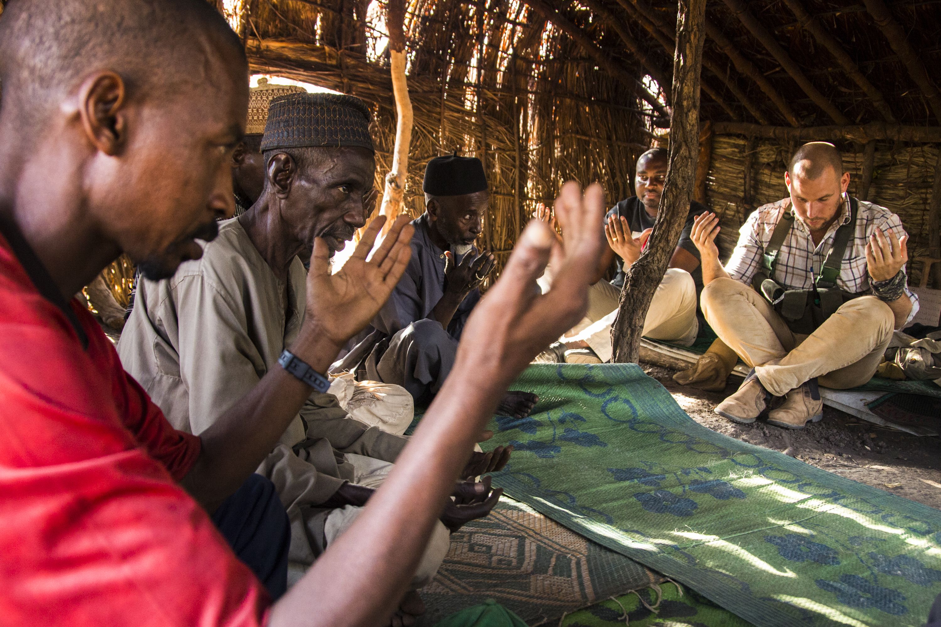 An imam leads prayers at the end of a meeting between Chinko park manager David Simpson and the elders of a community displaced by violence into the remote wilds of the reserve. Image by Jack Losh. Central African Republic, 2018.