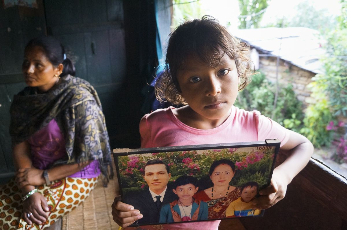 Lozan B.K., 9, holds a digitally-altered photo of her family. Her father, Giri Prasad B.K., who was added to the photo, went to Qatar as a migrant worker before Lozan was born. He was injured there in a road accident and has been in a vegetative state since 2011. Image by Yam  Kumari Kandel. 2016. 