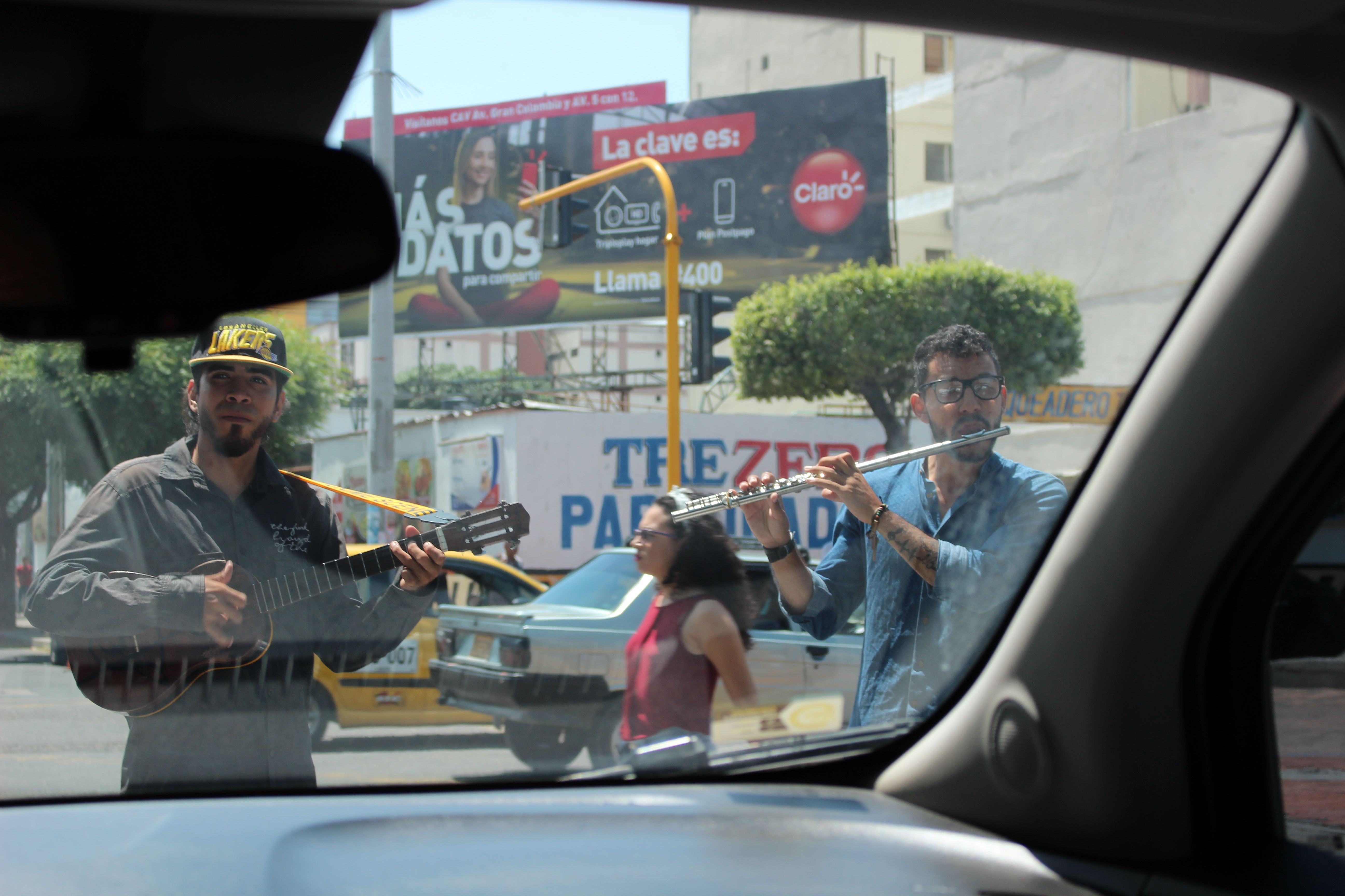 Venezuelans perform at a stoplight. One of them plays a popular Venezuelan instrument known for its four strings, a cuatro. Image by Mariana Rivas. Colombia, 2019.