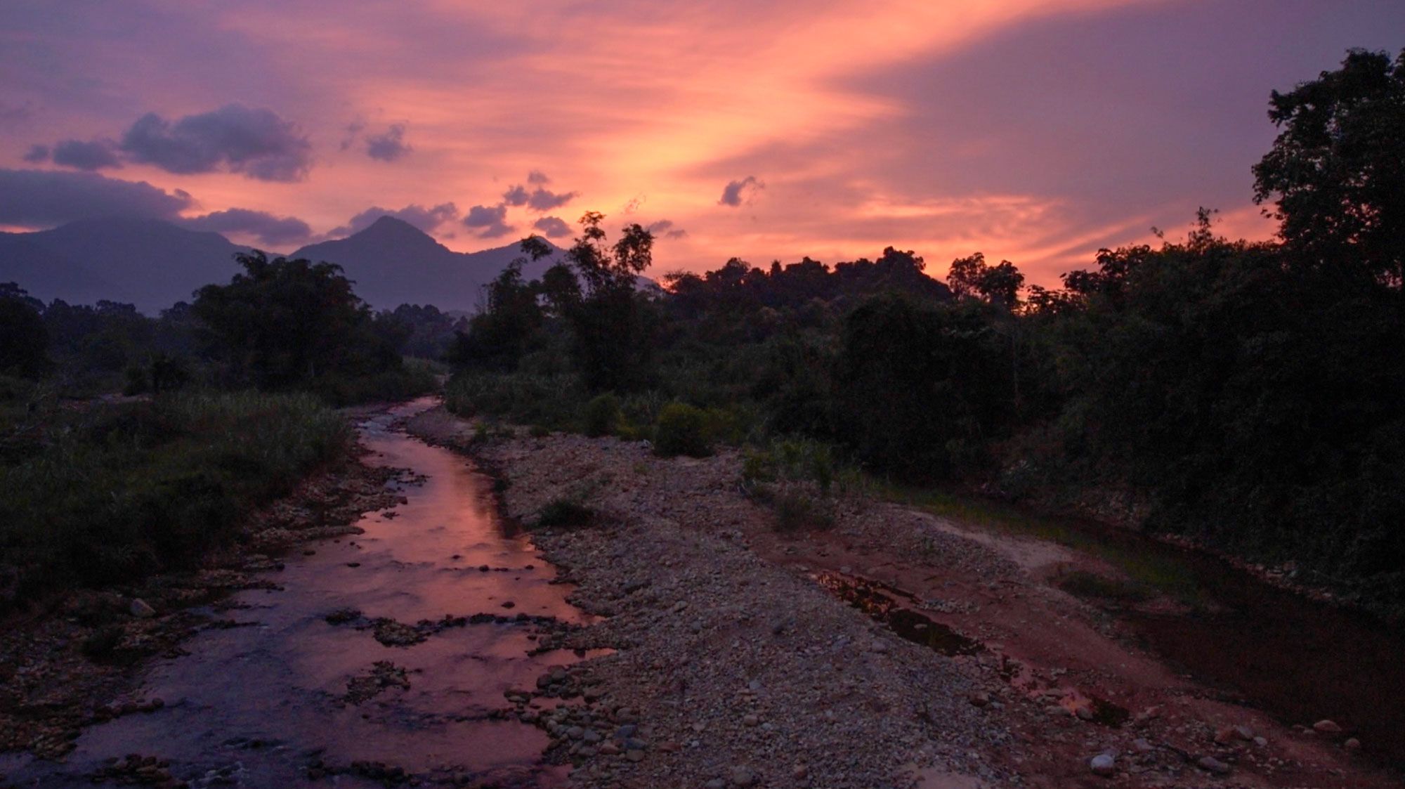 A small river flows near the village of Lumar as the sun sets behind the 4889’ peak of Gunung Bawang.