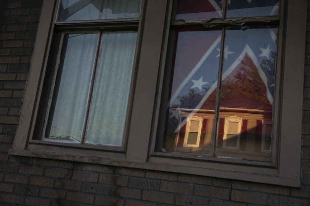 A confederate flag hangs in the window of a home of a young Black woman in Shawnee Ohio, on Tuesday, July 28, 2020. Confederate flags have become a symbol of a certain America: white, often rural, sometimes southern, normally conservative. This time, though, it turned out to be a young Black woman who was flying it. She said it was her way of "giving the finger" to everyone, including white Southerners who believe they control the flag and its symbolism. Image by Maye-E Wong/AP Photo. United States, 2020.