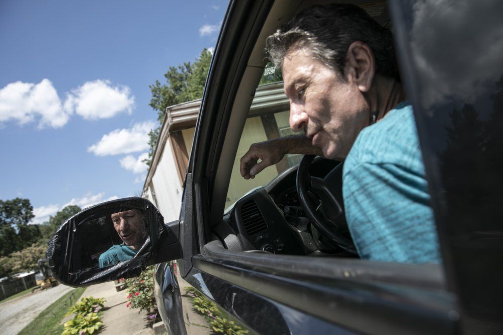 Larry Steele parks his truck outside his mother's trailer home in New Marshfield, Ohio, on Tuesday, July 28, 2020. Larry is a quiet man with a gravelly voice and armfuls of tattoos, a couple of them illegible because "the guy doing the tattoo was drunk." A bout with COVID-19, including three weeks in the hospital, has left him rail thin. He and his partner, Penny Hudnall, survive by supplementing her disability payments with foraging in the woods for wild foods—walnuts, hickory nuts, paw paws, persimmons, spiceberries—and selling them to local farmers. Image by Wong Maye-E/AP Photo. United States, 2020.