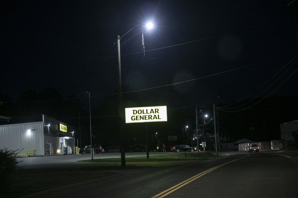 A Dollar General store sign is illuminated along a street in Zanesville, Ohio, on Sunday, July 26, 2020. Often, the most crowded parking lots are at the ubiquitous Dollar General and Family Dollar stores, signposts of financial hardship. Image by Wong Maye-E/AP Photo. United States, 2020.