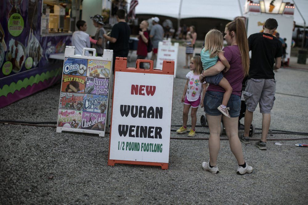Visitors to the Perry State Fair walk past a food stand selling the “Wuhan Weiner,” Friday, July 24, 2020, in New Lexington, Ohio. Image by Wong Maye-E/AP Photo. United States, 2020.