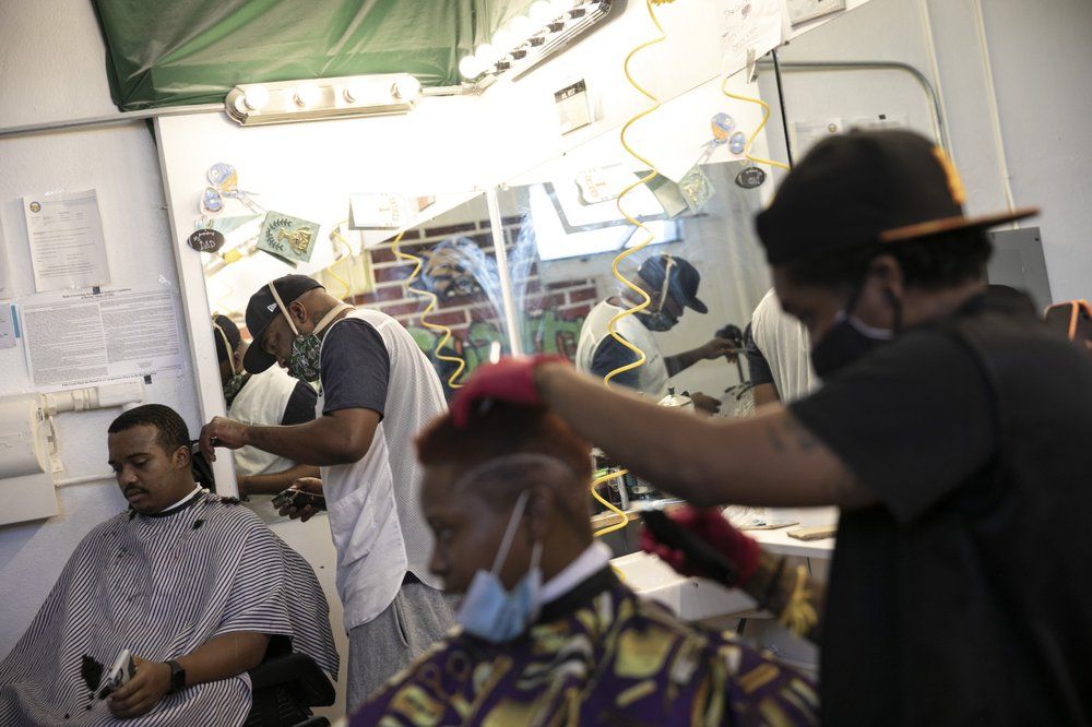 Geoffrey West, 34, second left, cuts the hair of customer Bayione Rogers, 22, at the Court Barbershop in Athens, Ohio, on Wednesday, July 29, 2020. West, 34, runs the establishment serving the city's Black community on the third floor of an old downtown office building. West likes Athens, and said he's faced little direct racism since moving here three years ago. But he still believes there's plenty of racial misunderstanding, among both Black and white people, and he joined one of the handful of protests in the region against police violence over the past few months. Image by Maye-E Wong/AP Photo. United States, 2020.