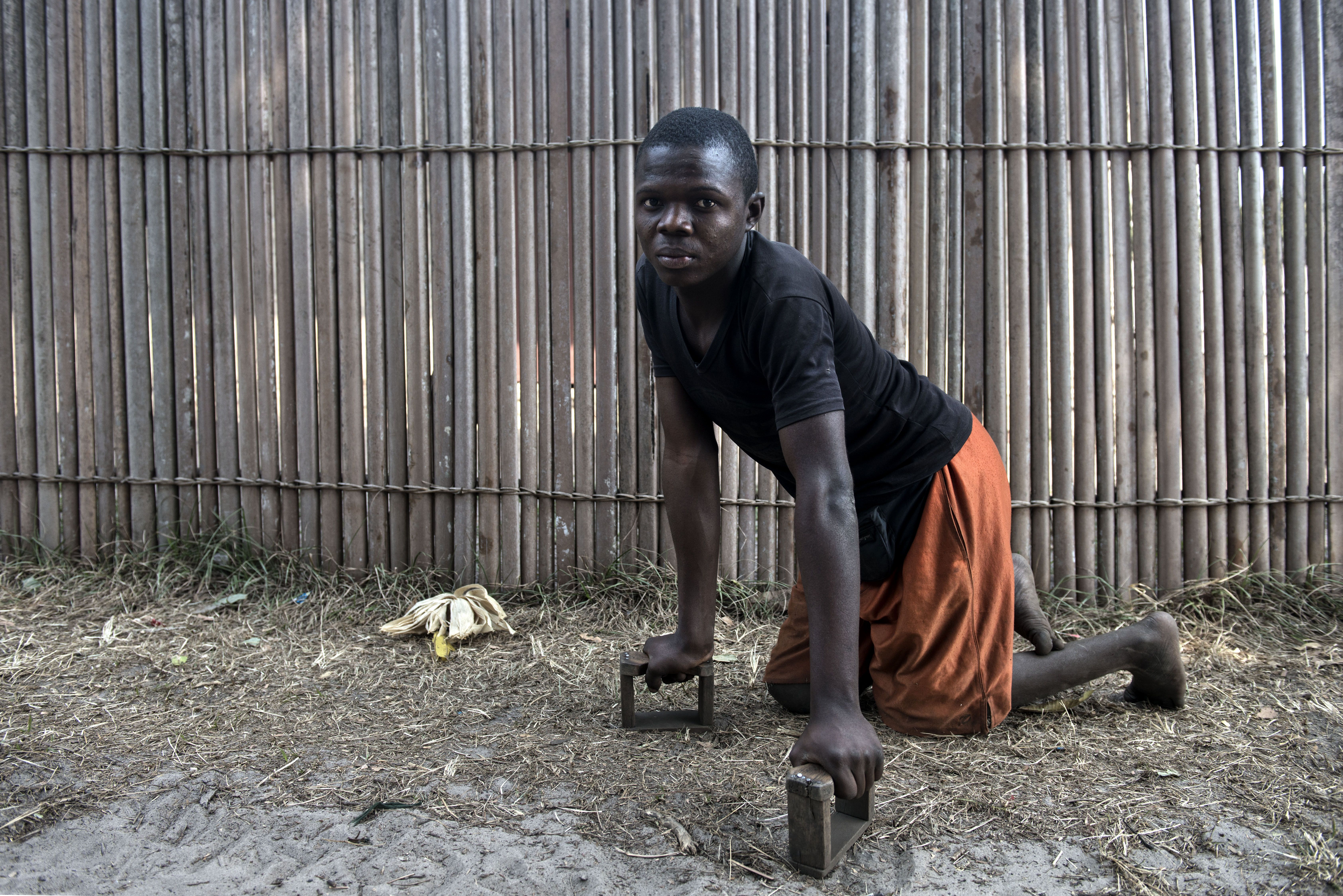 Again Kakene, 18, has had Konzo since 2002 and relies on wooden blocks to drag himself to the market and visit friends. He is the only one in his family with Konzo. Image by Neil Brandvold. DRC, 2016.
