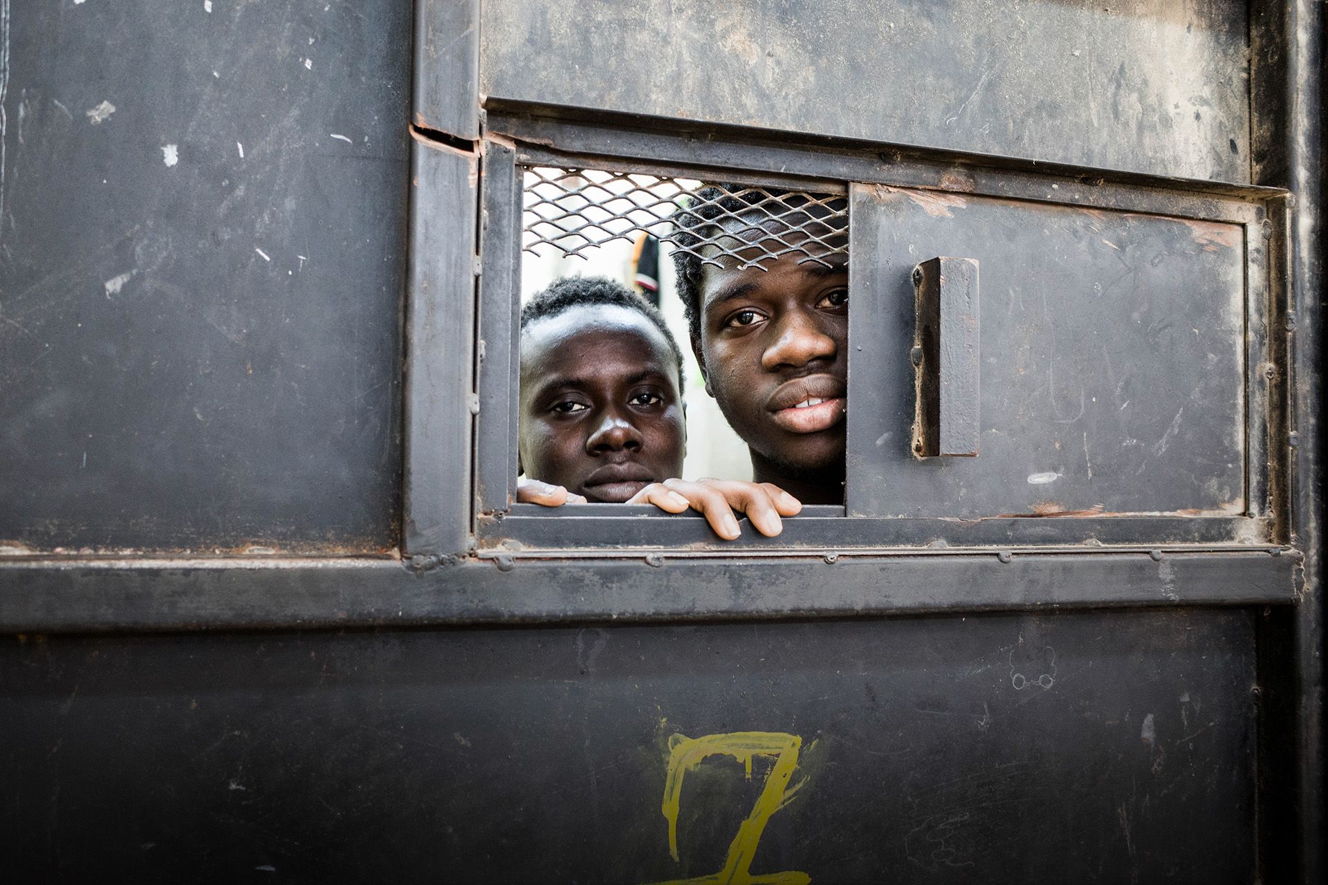 Detainees from West Africa peer out of their overcrowded cell in the al-Nasr detention center in Zawiya, Libya, where migrants intercepted by the Coast Guard in Zawiya are warehoused indefinitely. Image by Peter Tinti. Libya, 2017.