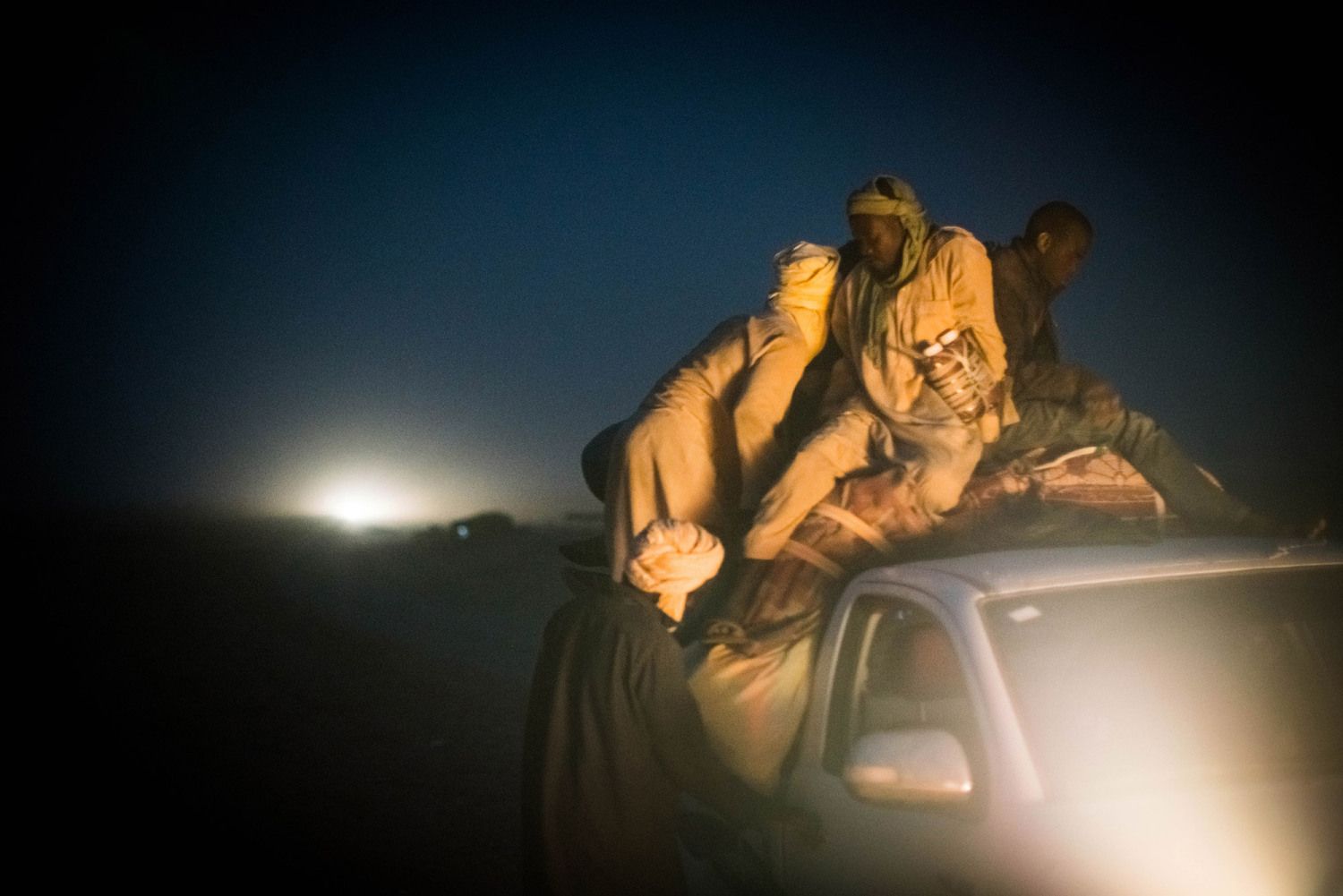 Migrants pile onto the back of a pickup truck bound for Libya on the outskirts of Agadez, Niger. The trip across the Sahara, where temperatures can soar above 120 degrees Fahrenheit, typically takes around three days. Image by Nichole Sobecki. Niger, 2017.
