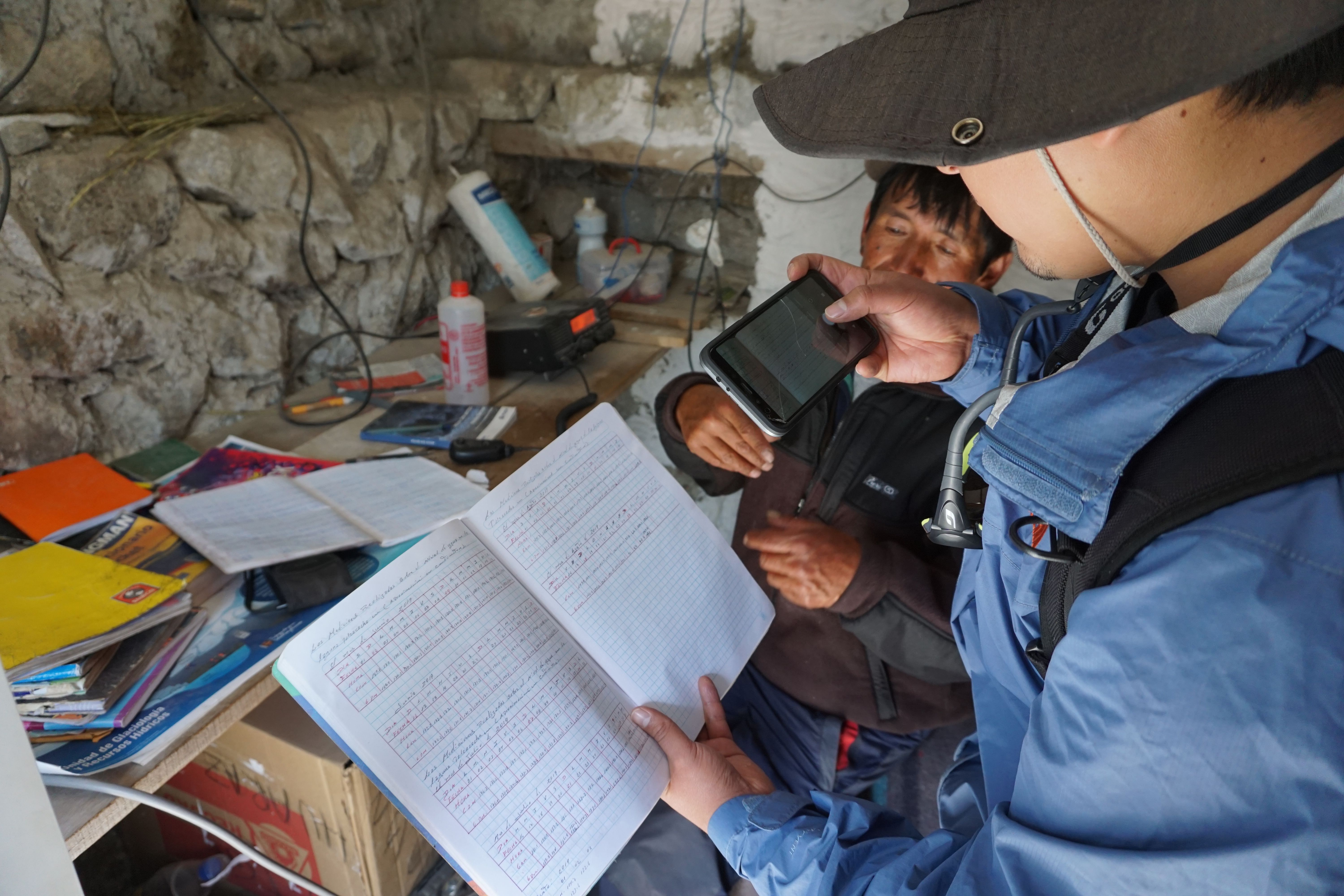 David Garay (front), an INAIGEM meteorologist, records data that Víctor Morales (back), a Lake Palcacocha Guard, gathered. Image by Audrey Fromson. Peru, 2019.