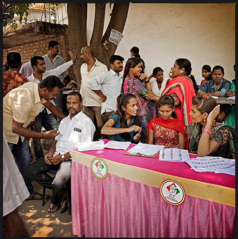 Intrepid Voters, India: Poll station helpers work a check-in table in Bengaluru during India’s 2019 general election. The 1950 Constitution of India, the former British colony’s founding national document, ensures suffrage to every adult Indian citizen regardless of “religion, race, caste, sex, or place of birth.” From the launch of the modern republic, in other words, Indian women have had the vote—and they exercise it. Image by Lynn Johnson. India, 2019.