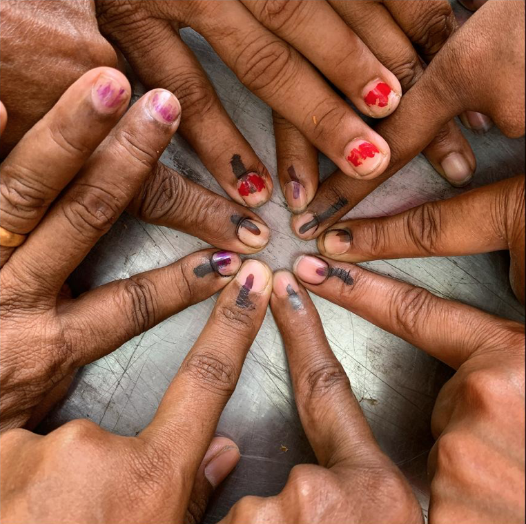 Intrepid Voters, India: At another polling station, women show off their fingers after casting their ballots; election officials mark voters’ nails with indelible ink in an effort to prevent repeats. Women still make up only 14 percent of the nation’s parliament, but they are enthusiastic voters. With all-women-staffed polling stations in every parliamentary district, some states report more women than men turning out on election days. Image by Lynn Johnson. India, 2019.