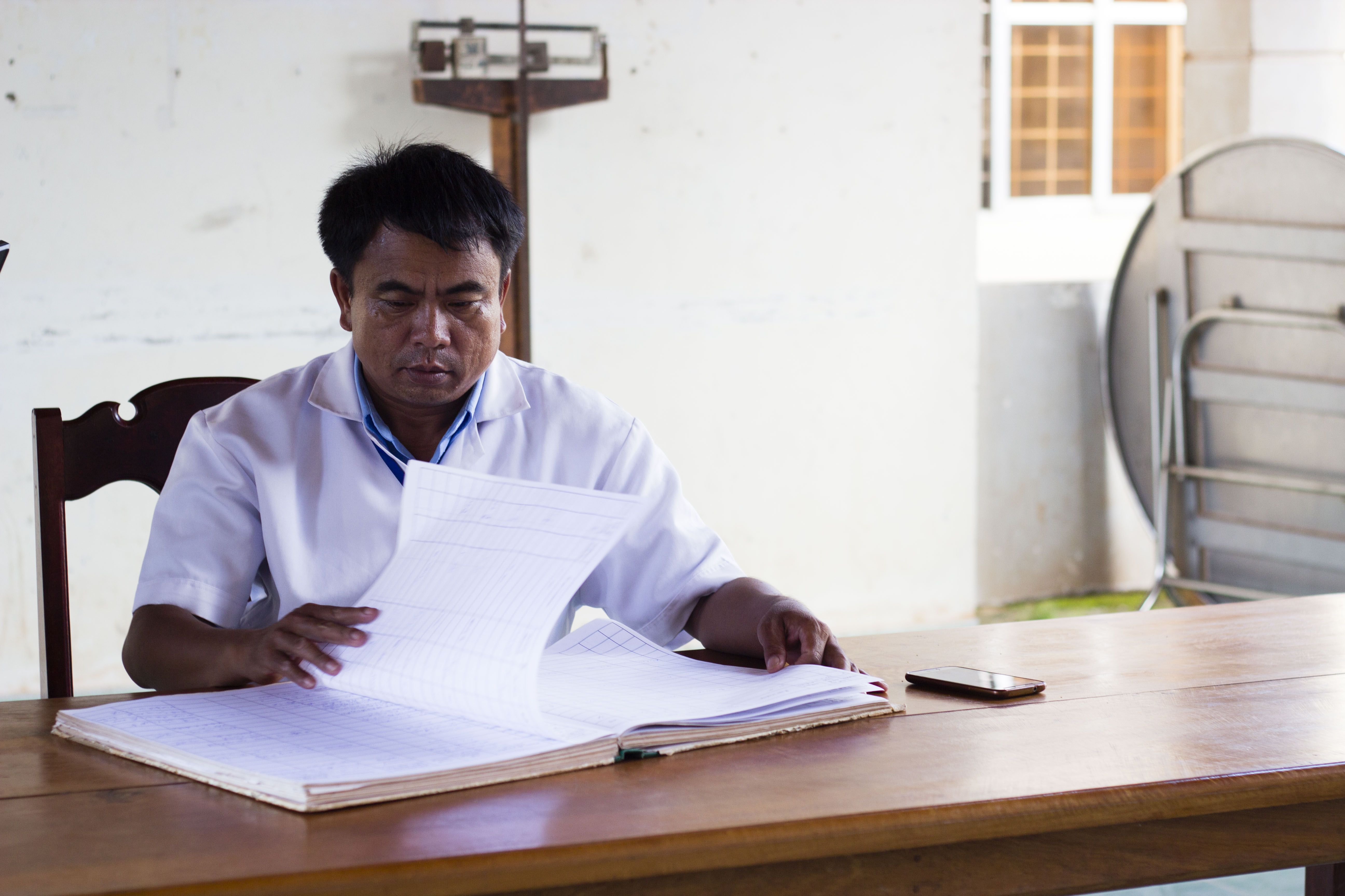 A doctor from the Thakhek Health Clinic reviews his records, telling the crew about recent UXO accidents. Image by Erin McGoff. Laos, 2017.