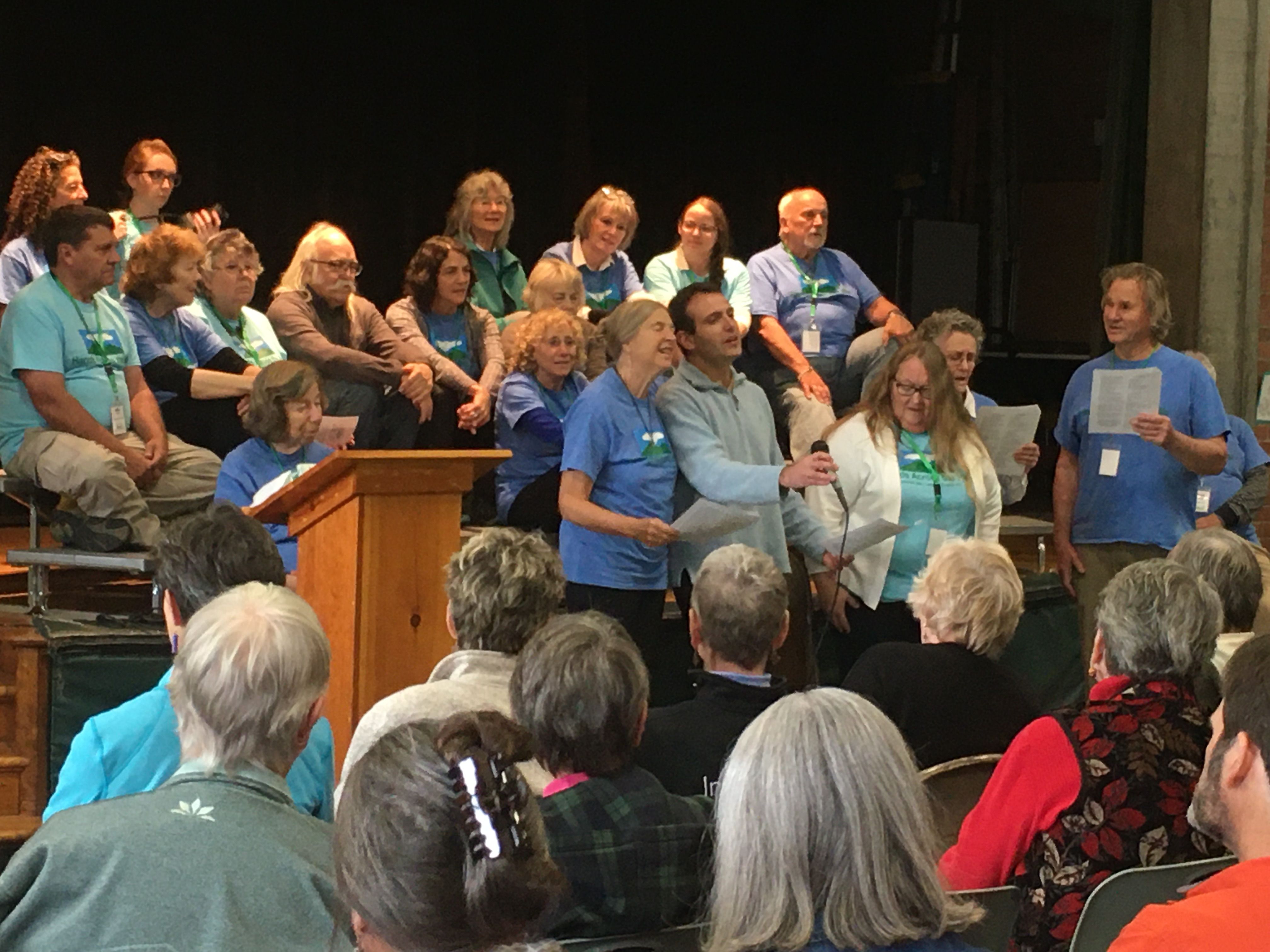 Hands Across the Hills participants sing at public forum in Leverett Elementary School’s auditorium as other group members from Kentucky and Leverett look on. Image by Richie Davis. United States, 2019.