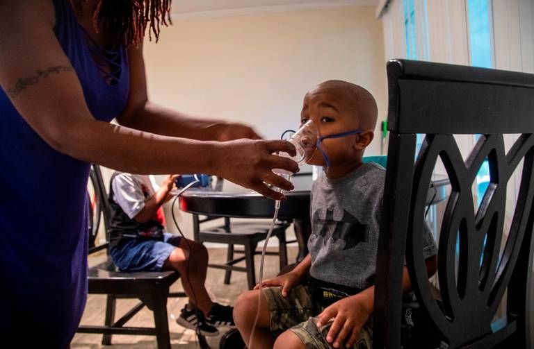 Vantisha Williams, left, adjust a nebulizer mask on the face of her 4-year-old son Jonathan, right, as he and his twin brother Jeremiah receive nebulizer treatments for asthma at their home in Bayboro Thursday, Aug. 20, 2020. Eastern North Carolina has more people making trips to hospital emergency departments for asthma treatments than in any other part of the state, researchers at East Carolina University reported. Image by Travis Long / The News & Observer. United States, 2020. 