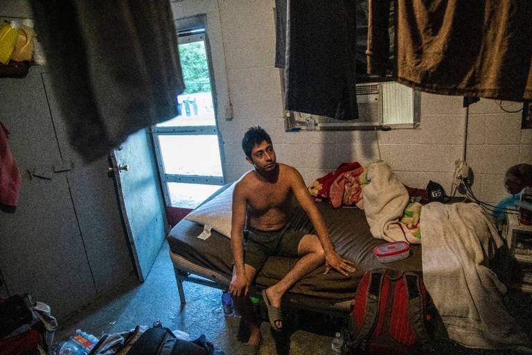 A farmworker named Javier sits inside his living quarters as clothes dry from the ceiling at a Johnston County farmworker camp Thursday August 27, 2020. Image by Travis Long. United States, 2020.