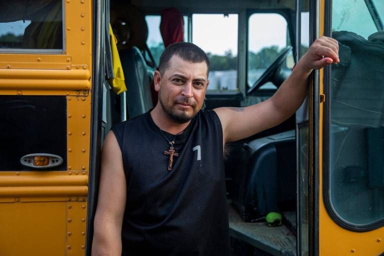 Jose, a tractor operator, stands outside a school bus used to transport farmworkers at a Johnston County farmworker camp Thursday August 27, 2020. Image by Travis Long. United States, 2020.