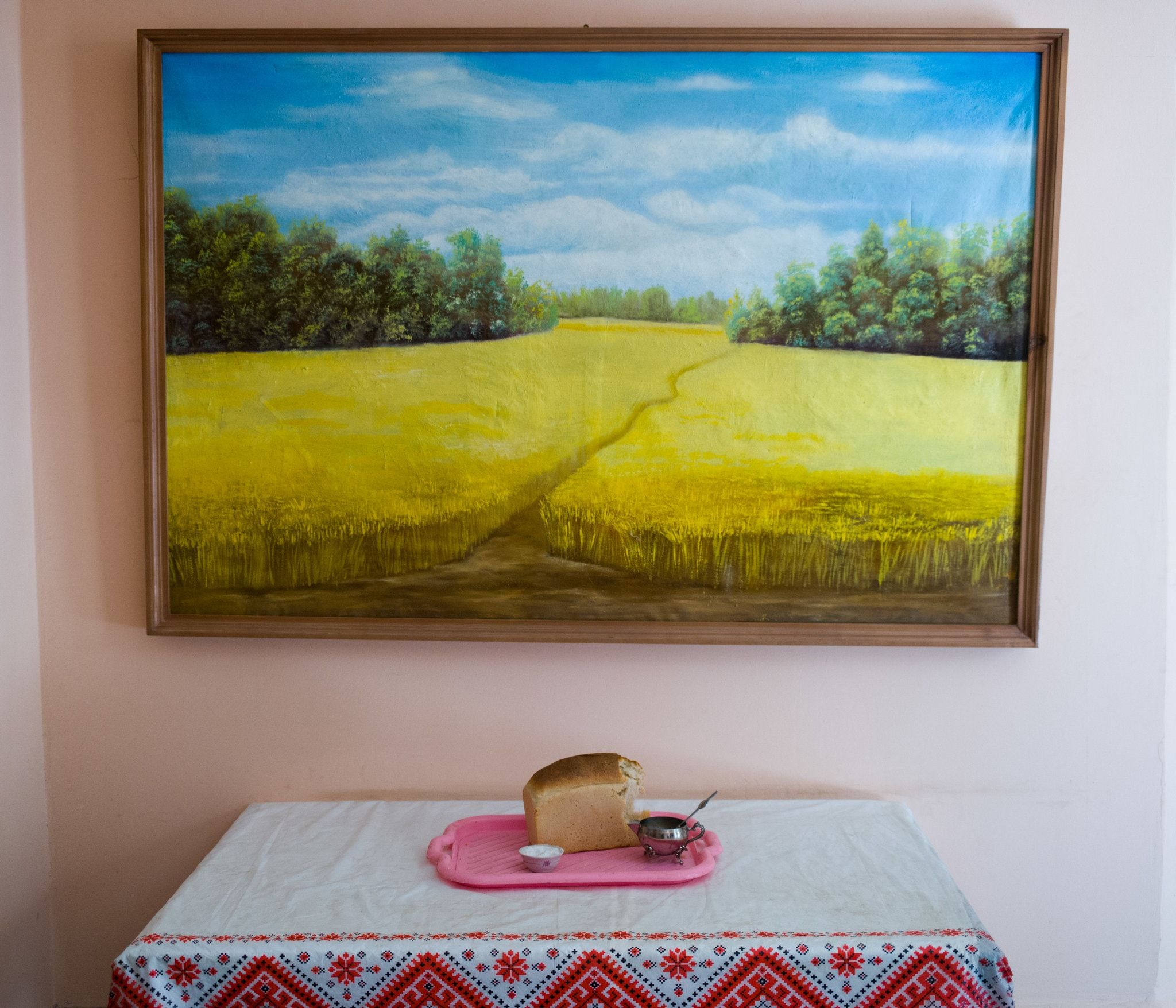 Below a painting of wheat, there is a table with bread and salt for visitors in a pretrial detention center. The prisoners make the bread. The painting is in the national colors. Image by Misha Friedman. Ukraine, undated.
