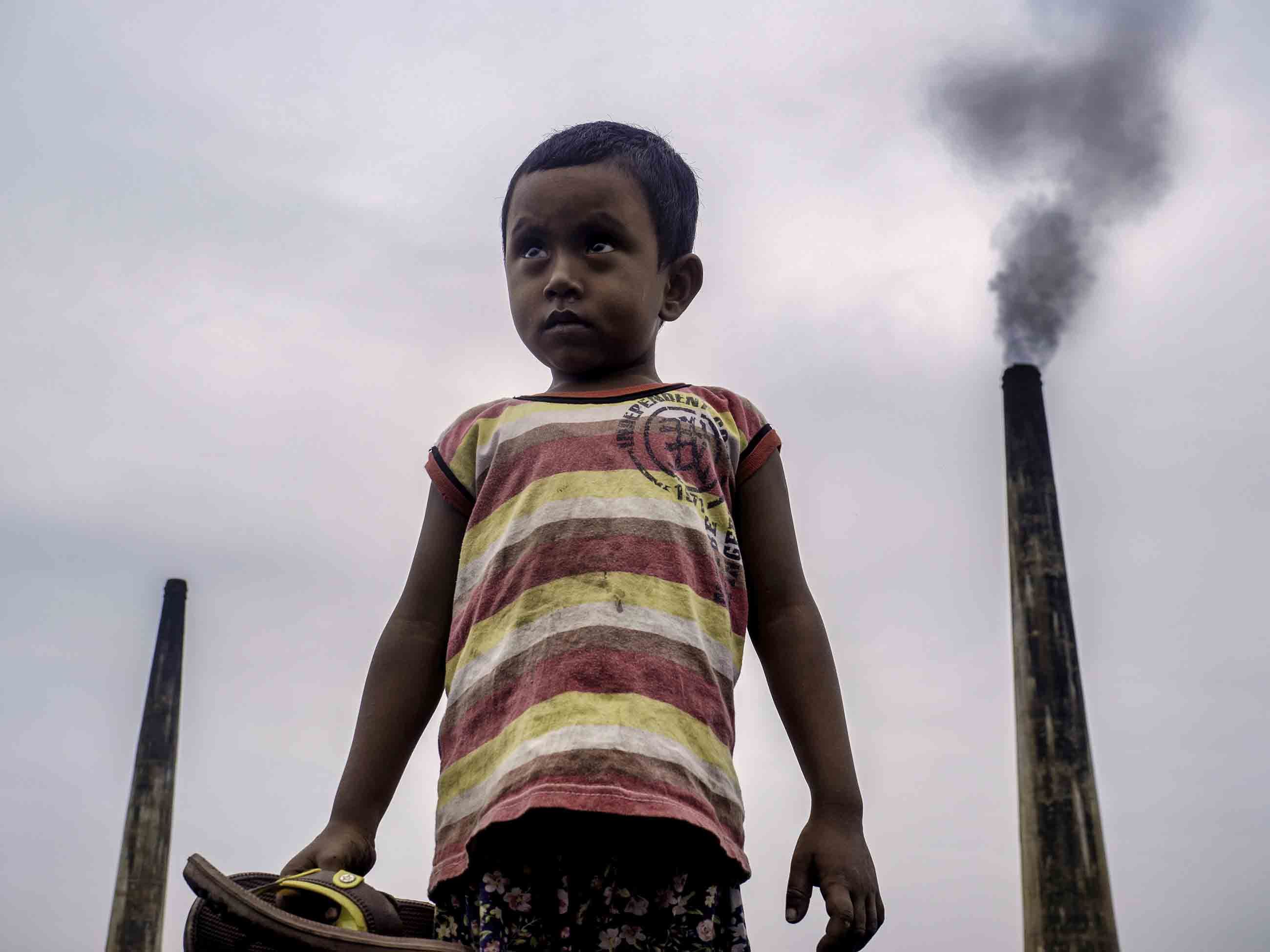 Four-year-old Nayem often plays atop large piles of coal used to fire kilns at a brick factory at the edge of Dhaka, Bangladesh. The chimneys from such factories contribute to some of the worst air pollution in the world. Image by Larry C. Price. Bangladesh, 2018.