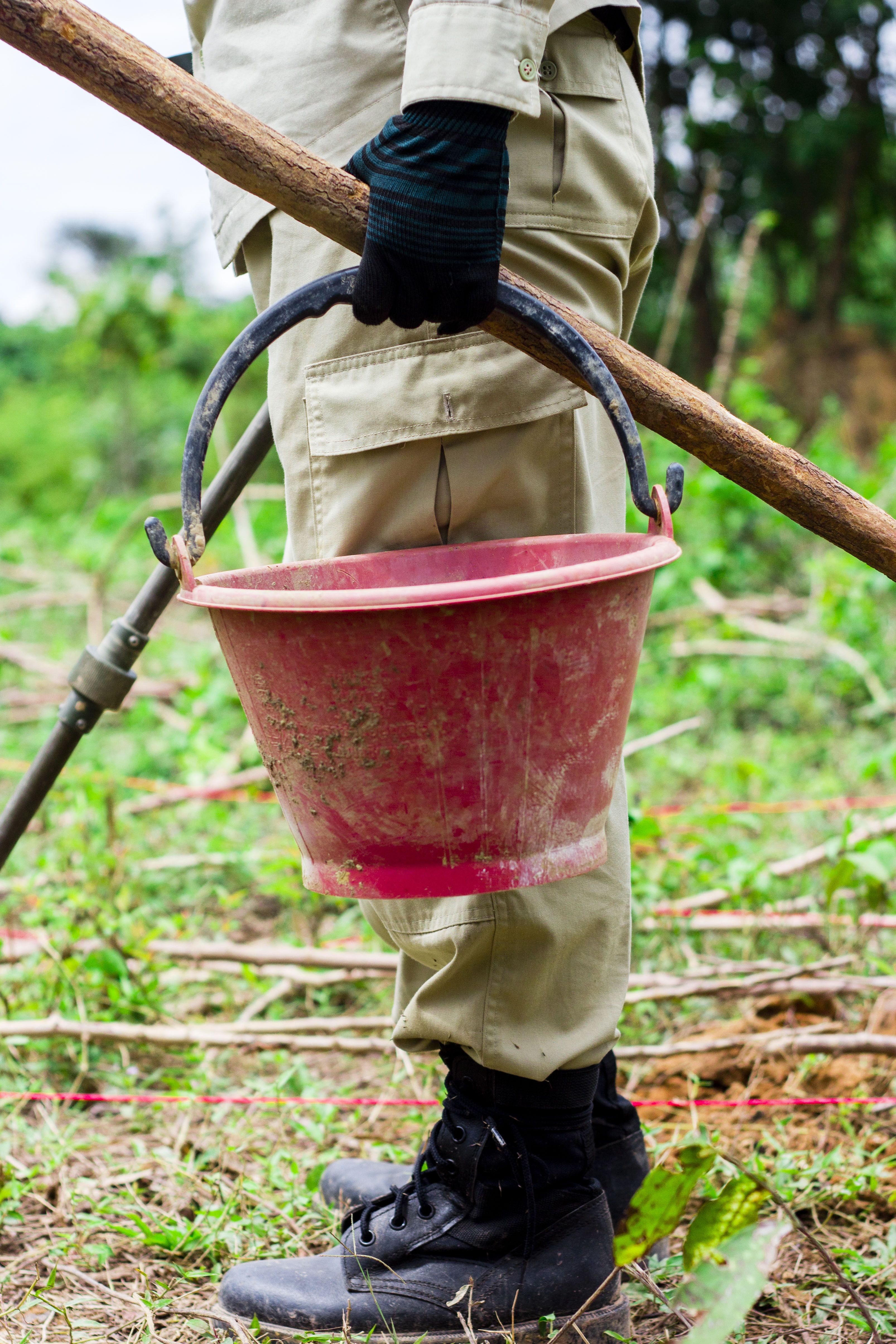 Phetsamay stands with the three instruments every UXO clearer is given: a bucket for scrap metal, a shovel for digging, and a metal detector. Image by Erin McGoff. Laos, 2017. 