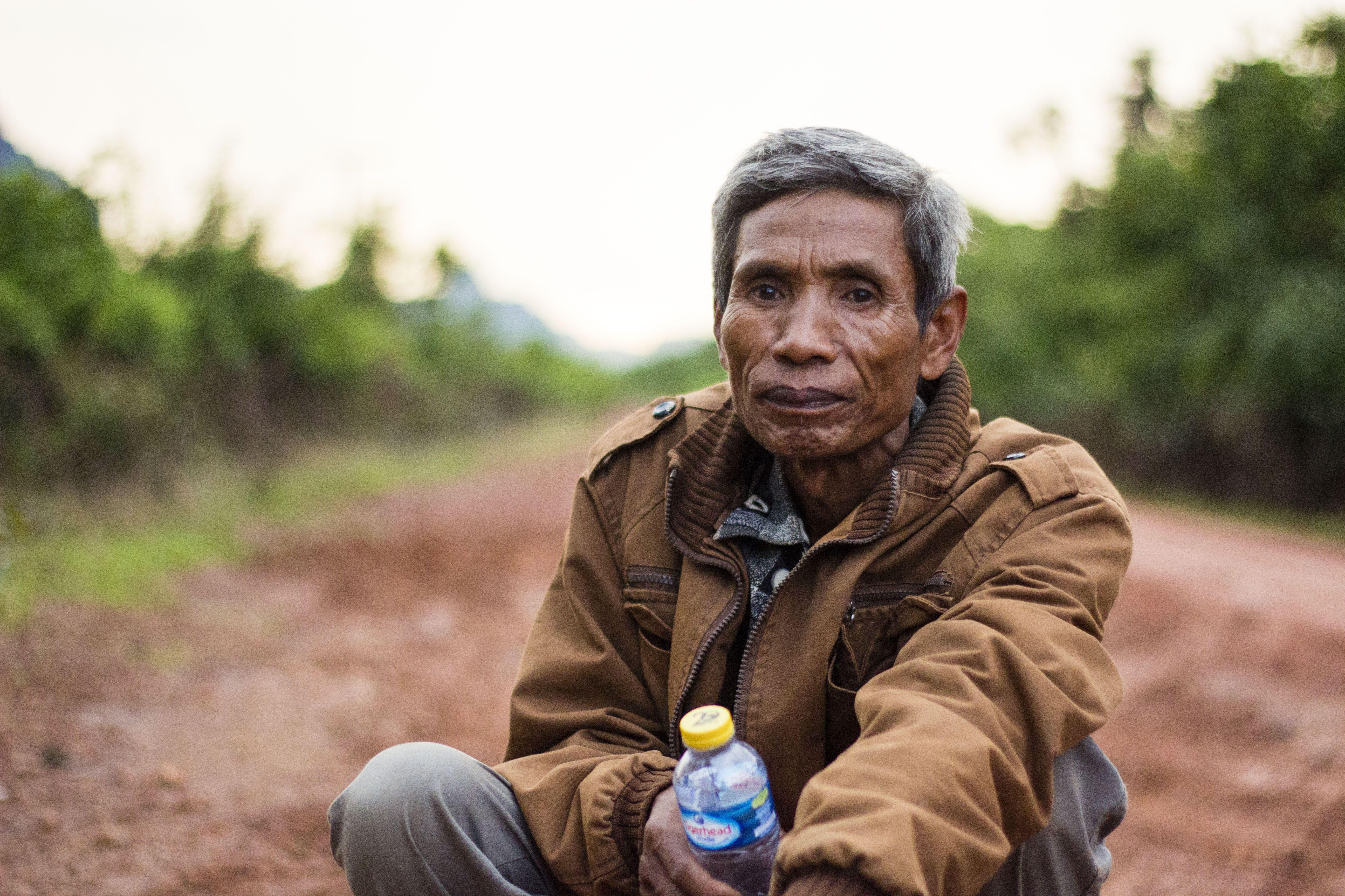 Lung Ki sits on the muddy road that leads to his village. Image By Erin McGoff. Laos, 2017.