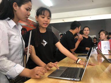 Young women attending the BarCamp ASEAN 2018 expo in Phnom Penh test the KOOMPI laptop. Image from Facebook/KOOMPI. Cambodia, 2018.