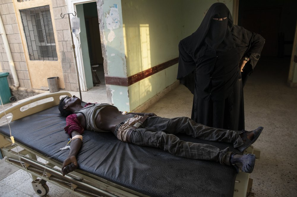 An Ethiopian Tigray migrant who was imprisoned by traffickers for months, lies on a gurney accompanied by a nurse at the Ras al-Ara Hospital in Lahj, Yemen. Nurses gave him fluids but he died several hours later. Image by Nariman El-Mofty. Yemen, 2019.