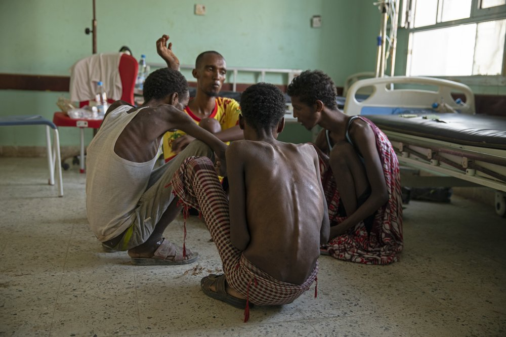 Ethiopian migrants, from center background to right, Gamal Hassan, Abdu Yassin, Mohammed Hussein, and Abdu Mohammed, who were imprisoned by traffickers for months, eat rice from a bowl on the floor, at the Ras al-Ara Hospital in Lahj, Yemen. They said they were fed once a day with scraps of bread and a sip of water when they were held. Image by Nariman El-Mofty. Yemen, 2019.